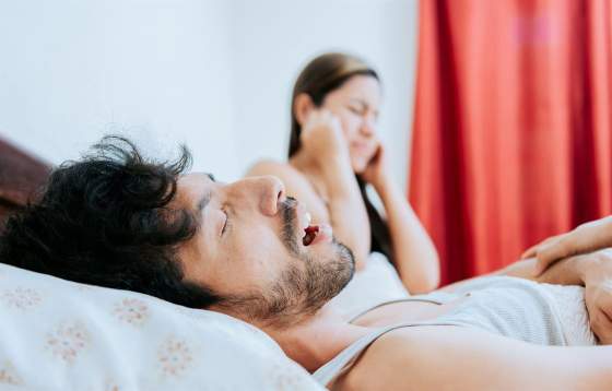 A man snoring in bed and wife covering her ears
